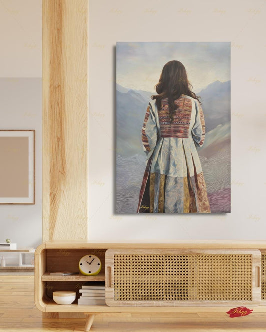 Back-view portrait of a woman with long dark wavy hair wearing a traditional Afghan embroidered dress with intricately paneled fabric in blue, rust, and earth tones, against a misty layered mountain landscape.