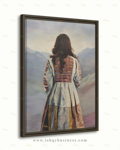 Back-view portrait of a woman with long dark wavy hair wearing a traditional Afghan embroidered dress with intricately paneled fabric in blue, rust, and earth tones, against a misty layered mountain landscape.