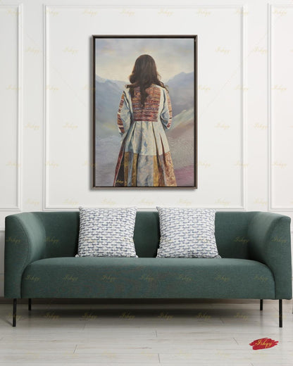 Back-view portrait of a woman with long dark wavy hair wearing a traditional Afghan embroidered dress with intricately paneled fabric in blue, rust, and earth tones, against a misty layered mountain landscape.